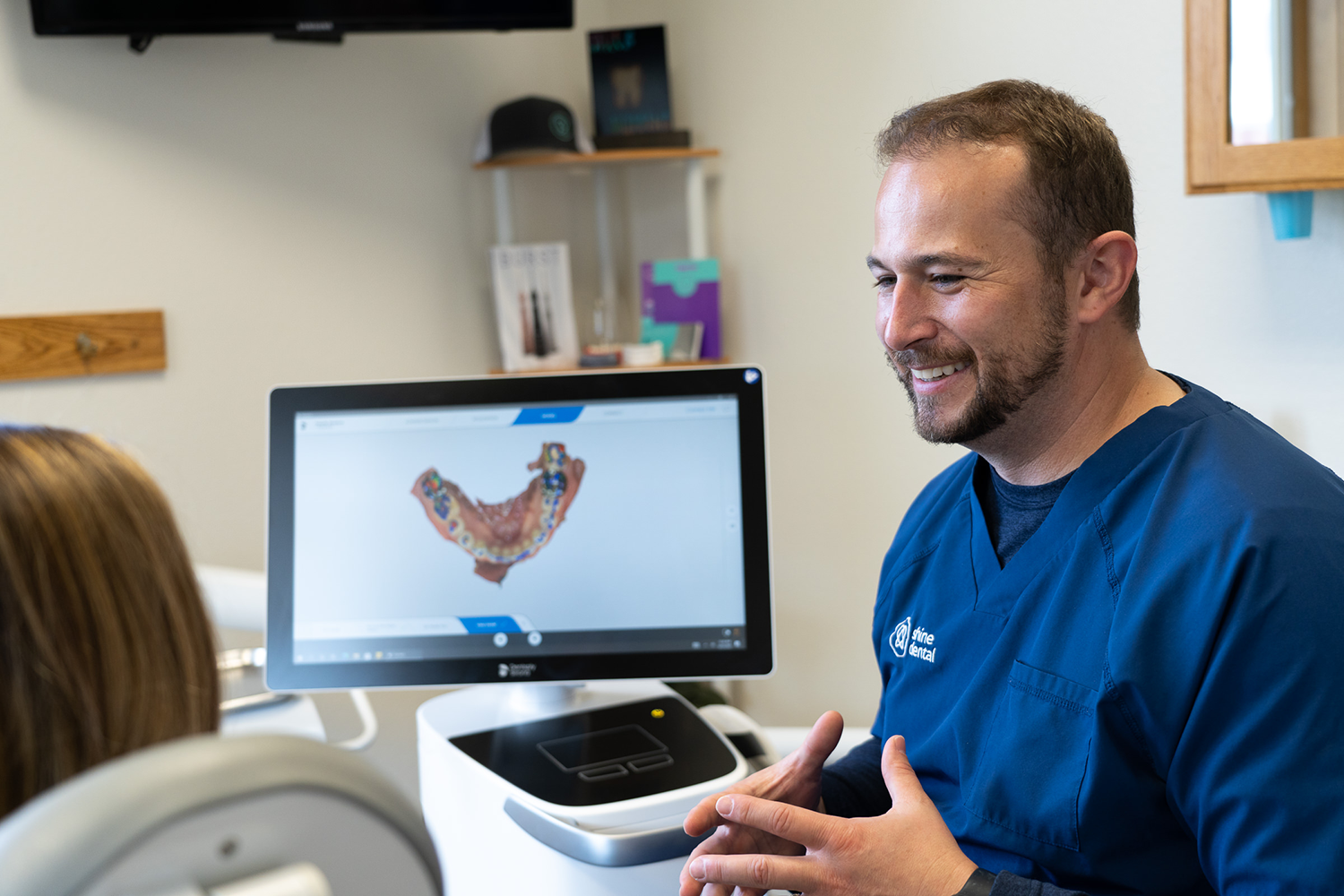 Dr. J, a dentist, is talking to a patient in front of a dental scanner screen.