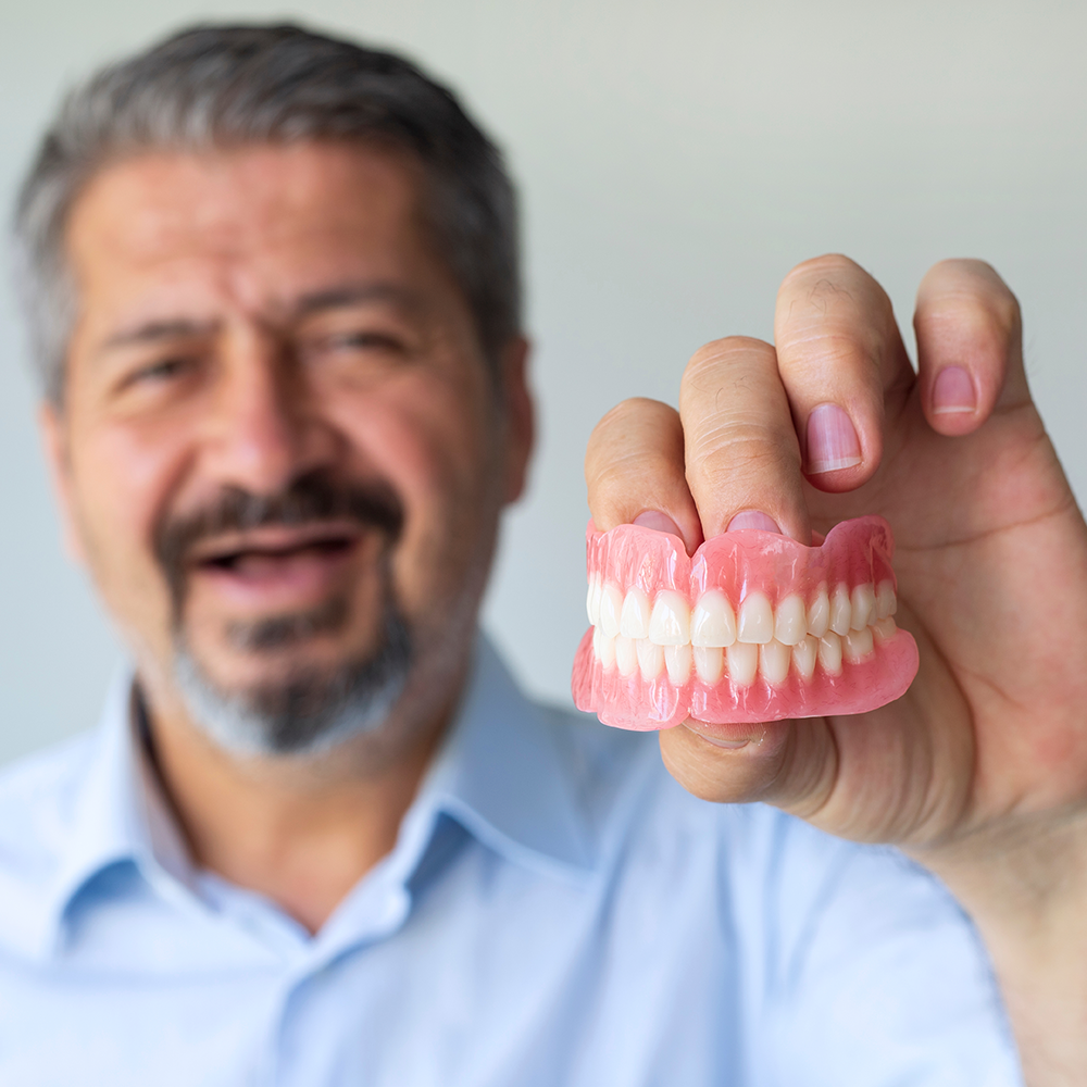 A man is holding a pair of dentures in his hand.