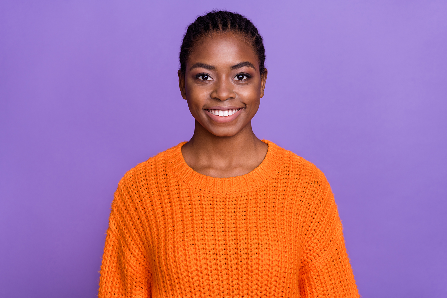 The woman is wearing an orange sweater and smiling.