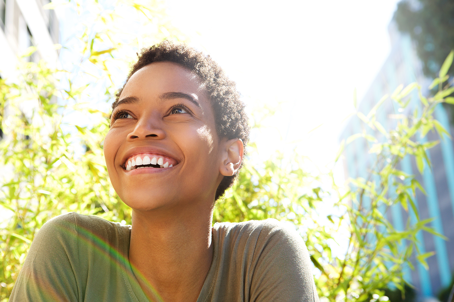 A woman is smiling and looking up at the sun.