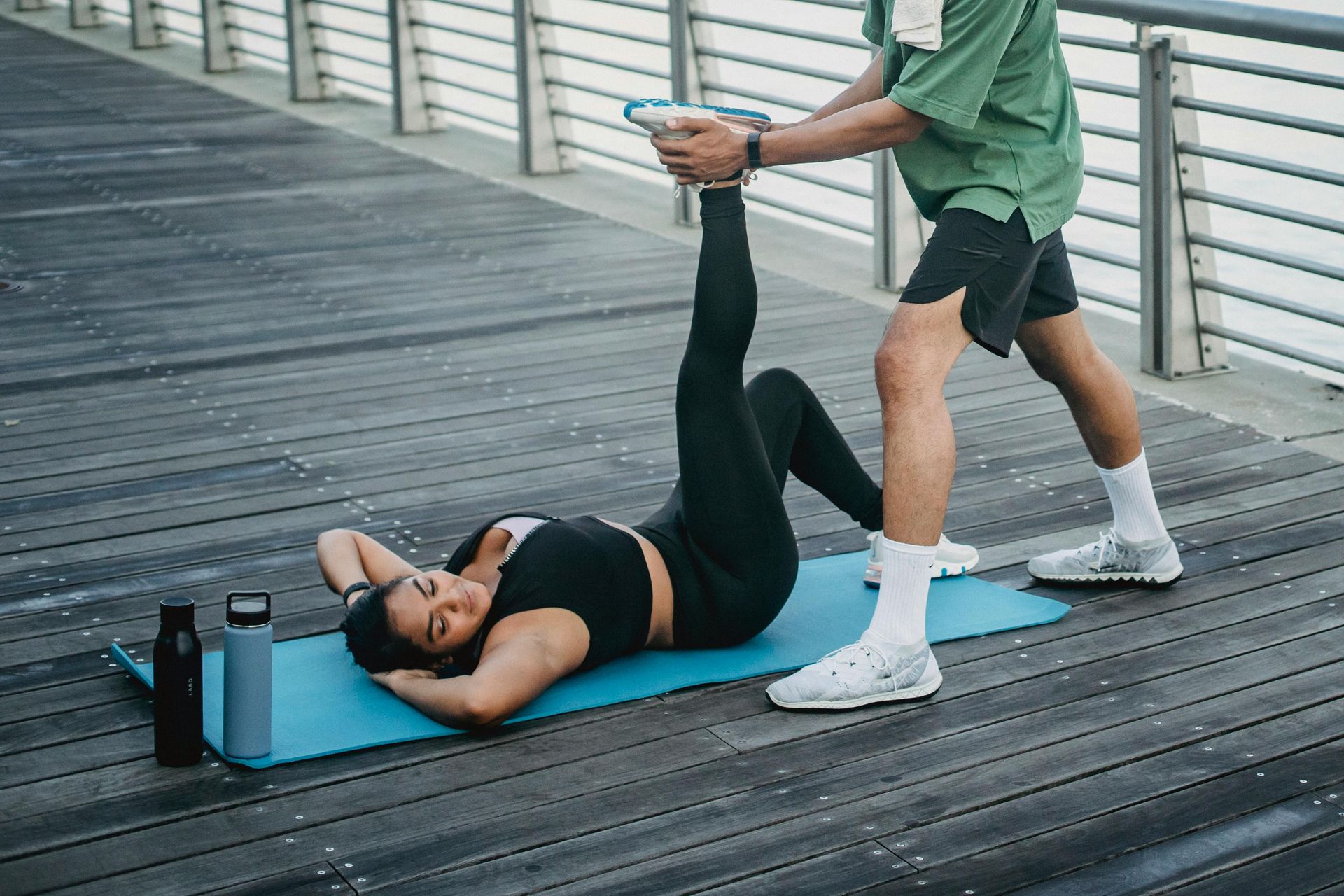 A man is helping a woman do exercises on a yoga mat.