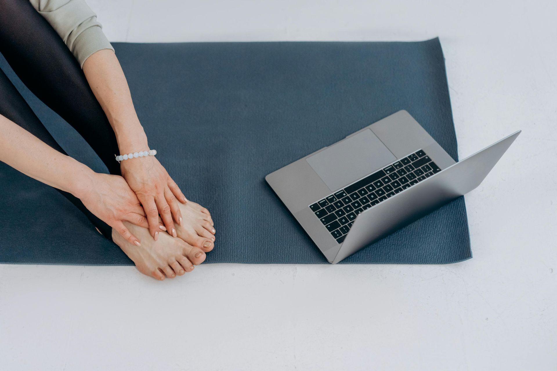 A woman is sitting on a yoga mat next to a laptop.