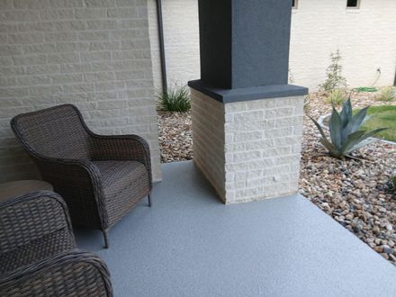 Porch with wicker chairs, textured gray floor, brick-style column, and landscaping.