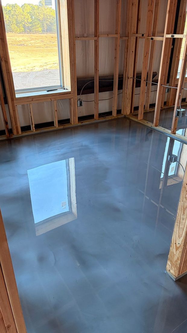 Room interior under construction with a reflective gray epoxy floor and wooden framing.