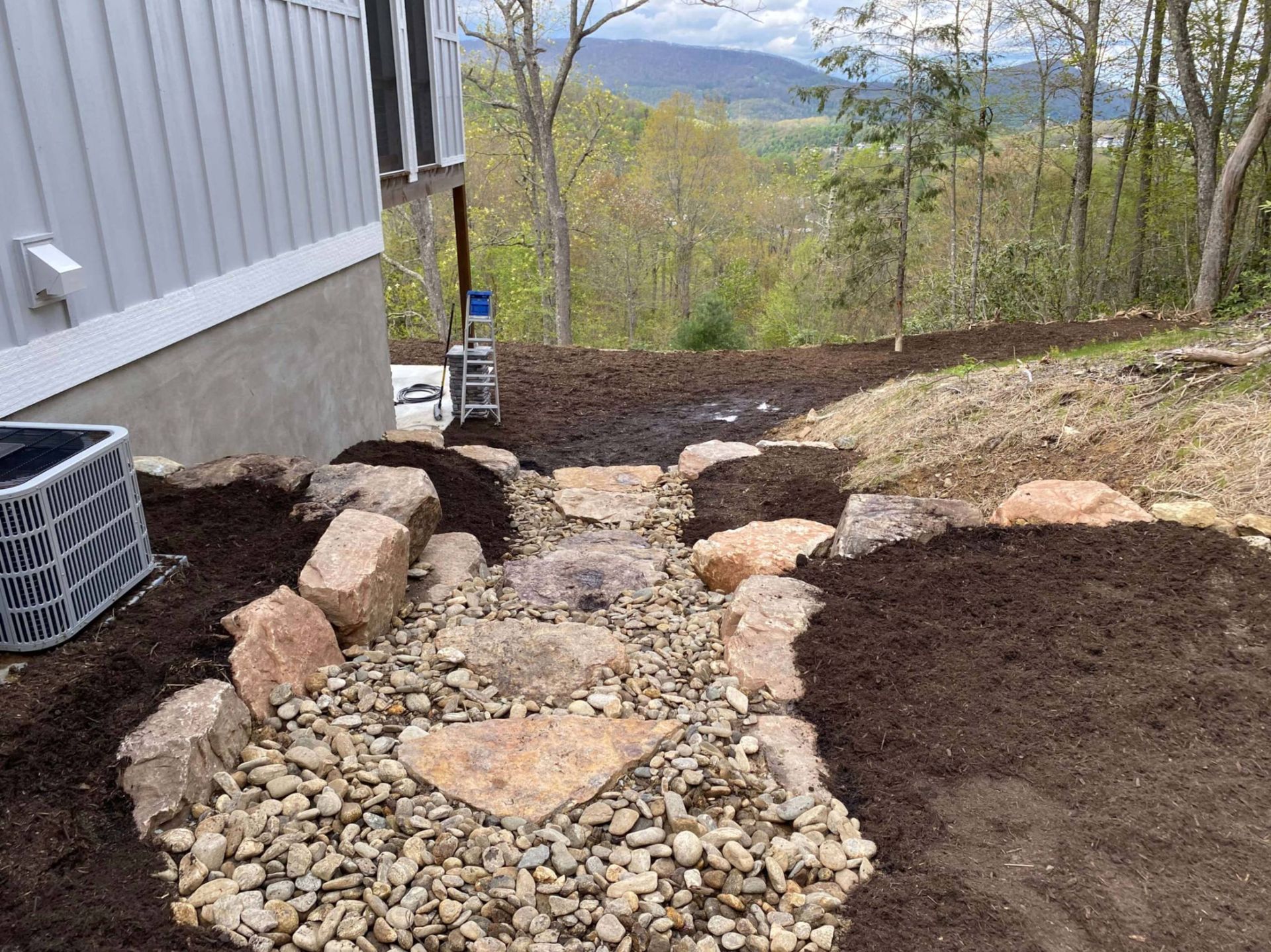 Stone path and large boulders in a landscaped yard, next to a building with a scenic mountain view.