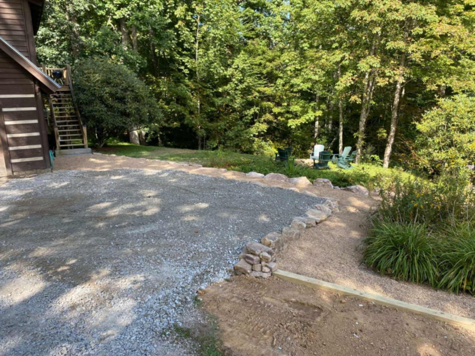 Gravel driveway beside a cabin. Gravel path leads to a grassy area with green trees in the background.