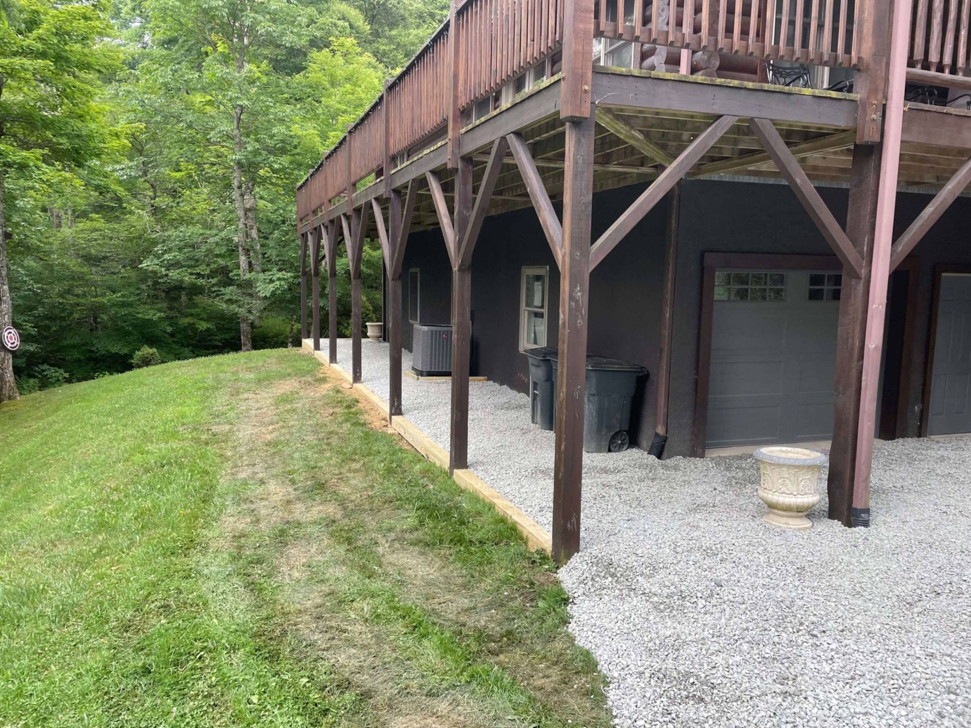 A building with a deck and gravel base on a hillside, with a grassy path leading up to it.