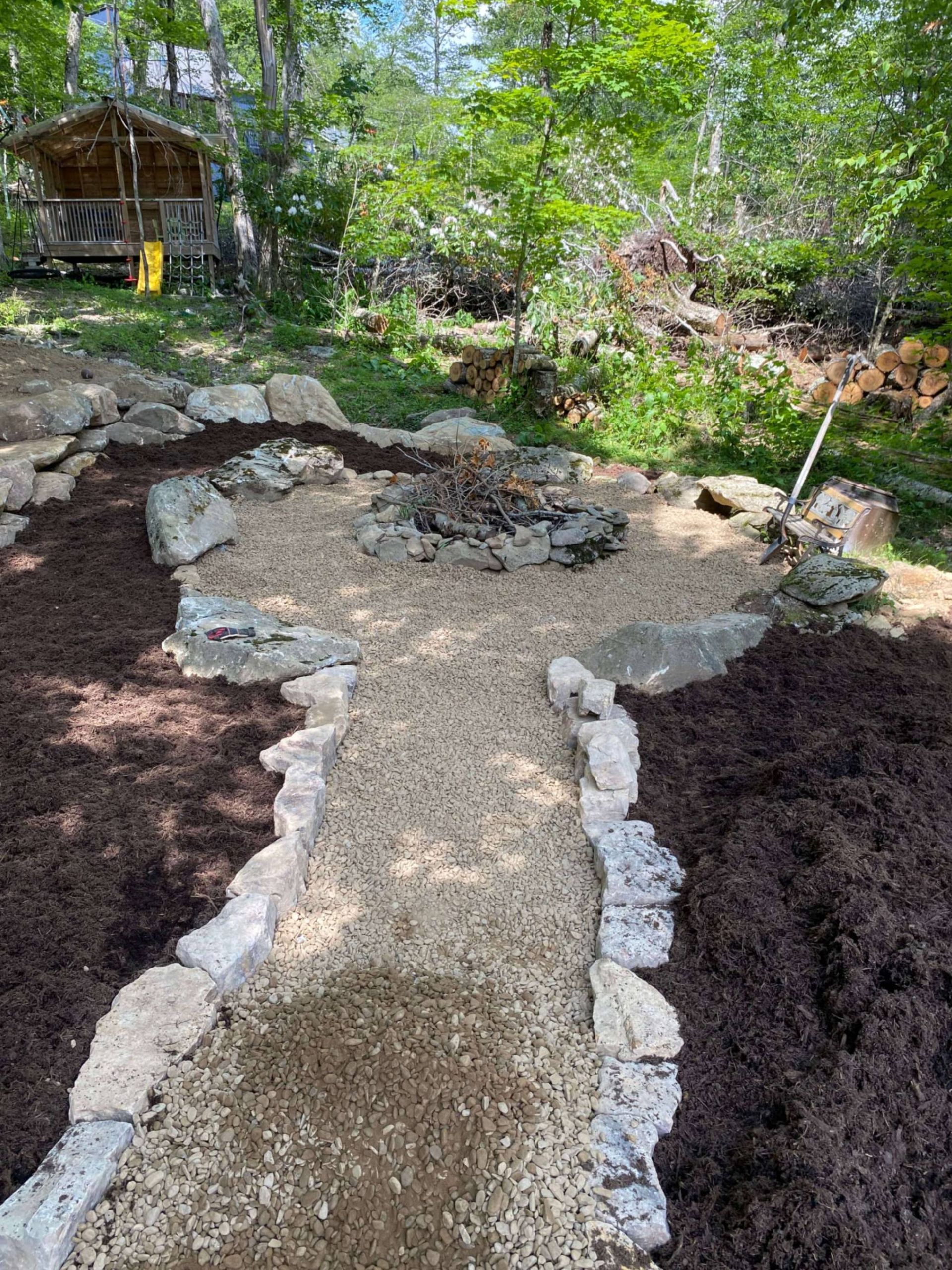 Path to a fire pit area with stone borders and mulch. A cabin is visible in the background.