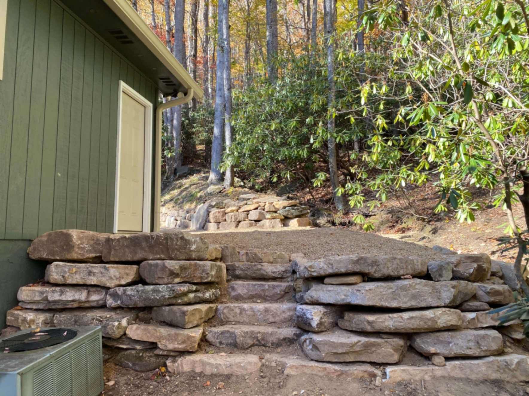 Stone steps leading up to a green building's door, set against a wooded hillside.