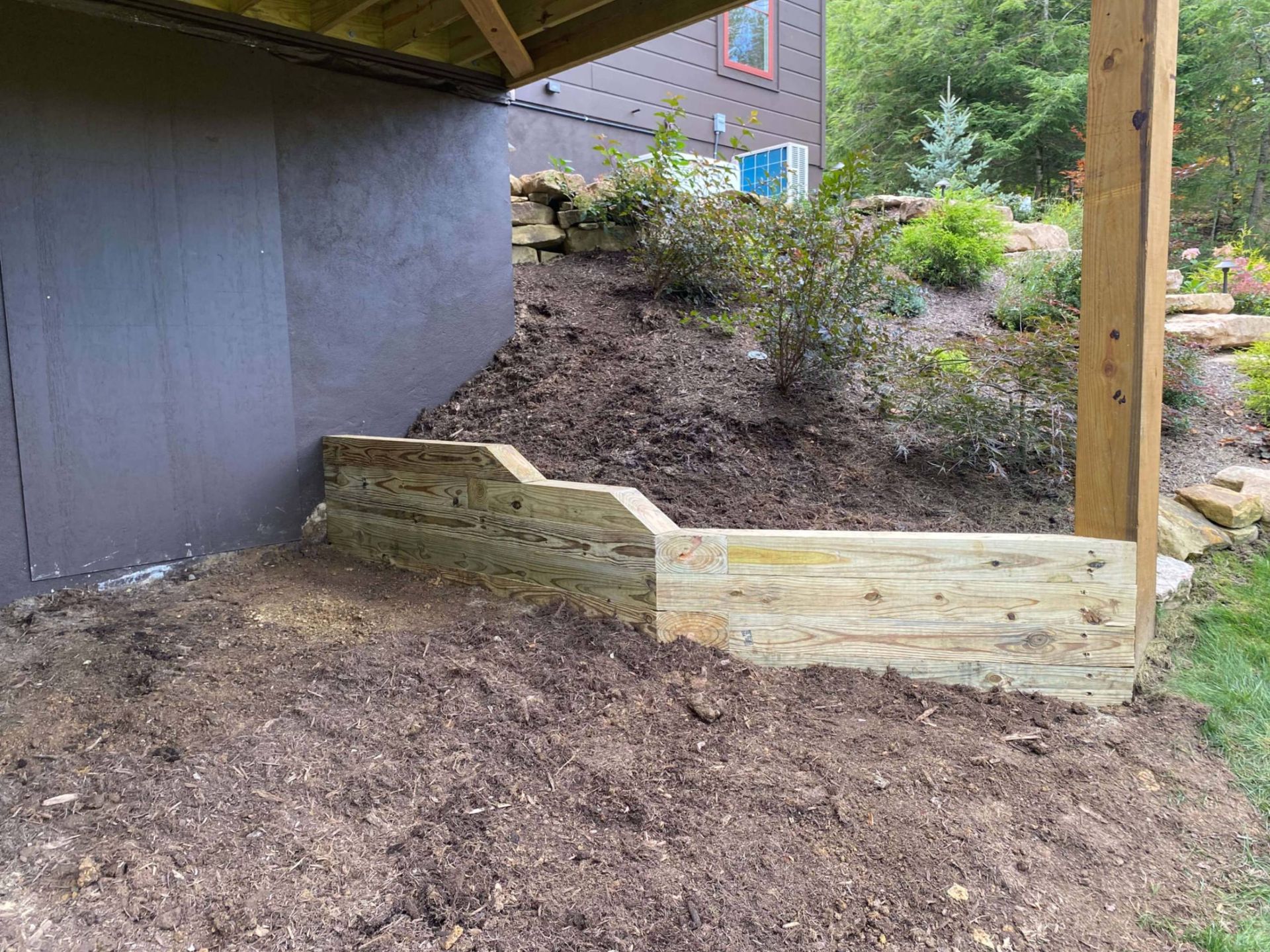 Wooden steps leading up to a house, surrounded by dirt and landscaping.