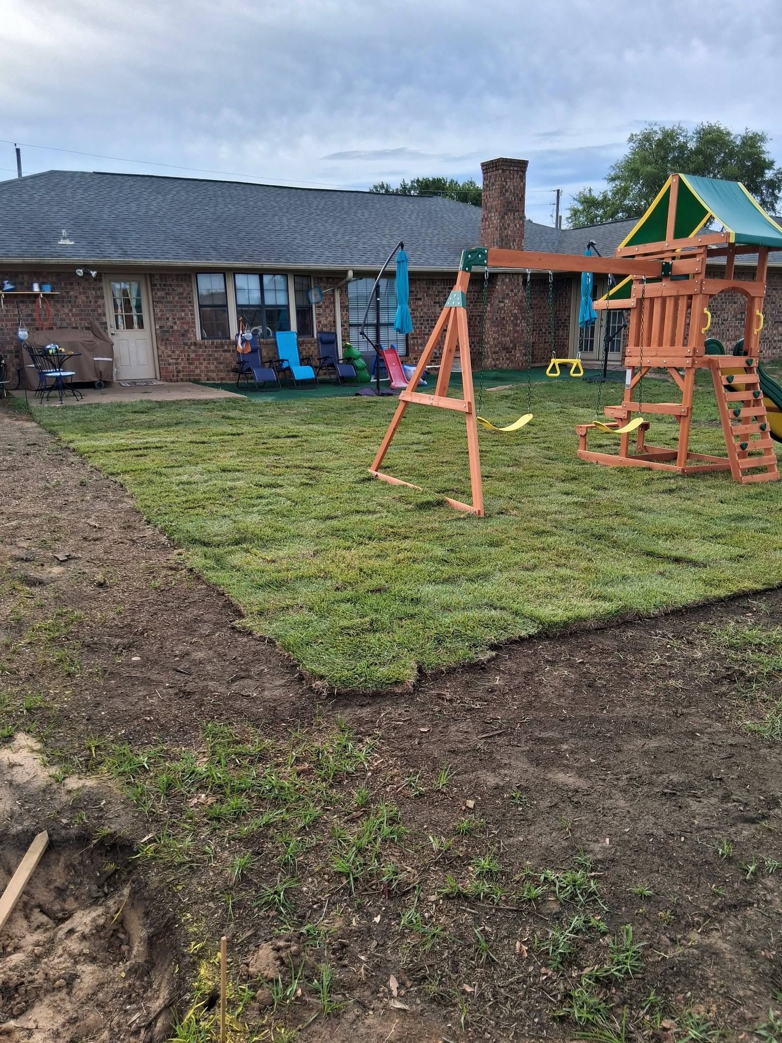 Backyard play area with swing set, wooden climbing structure, and a house in the background