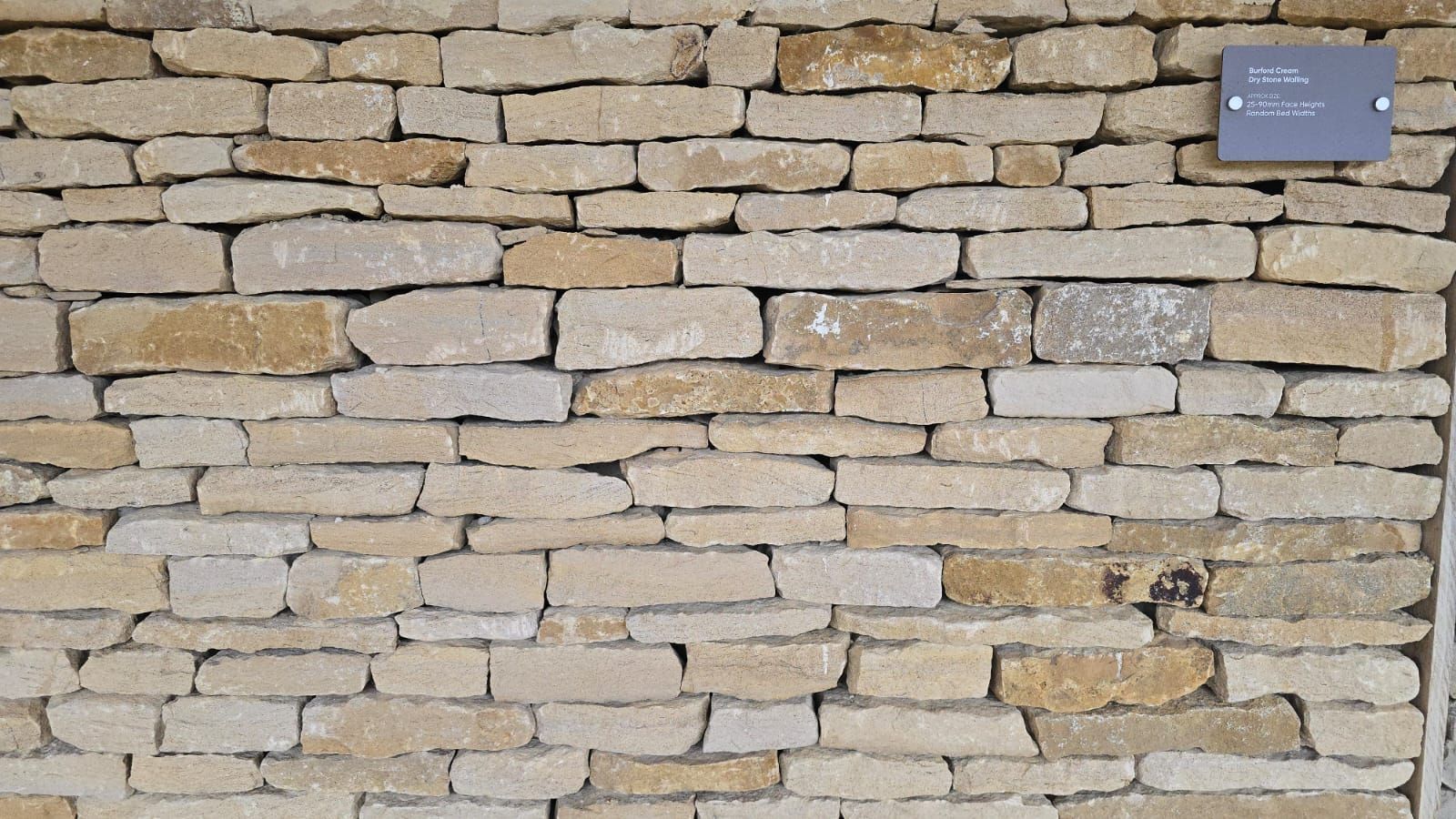 Stone wall with varying shades of beige and tan, with a small sign on the right.
