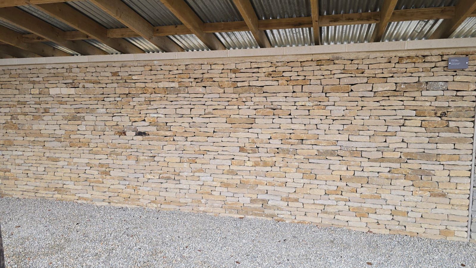 Stone brick wall with corrugated metal roof overhead and gravel ground.