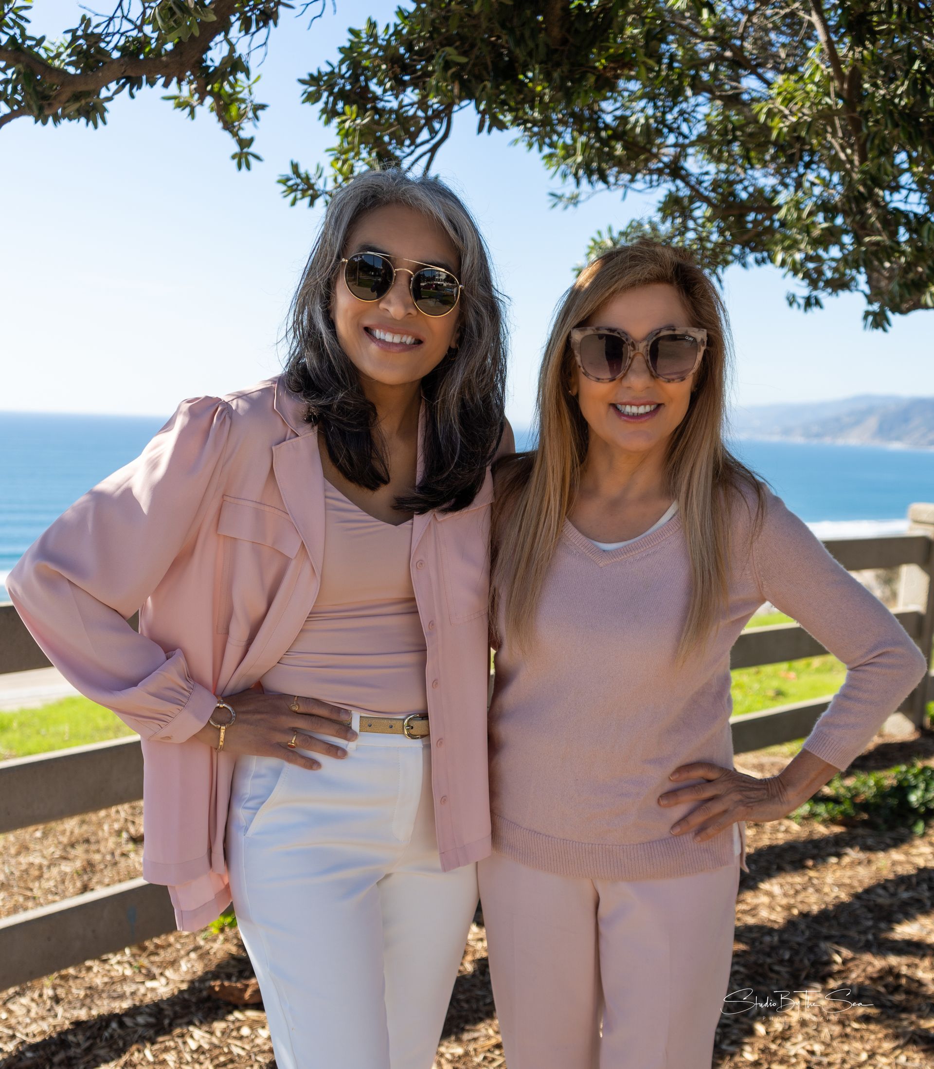 Two women are standing next to each other in front of a tree.