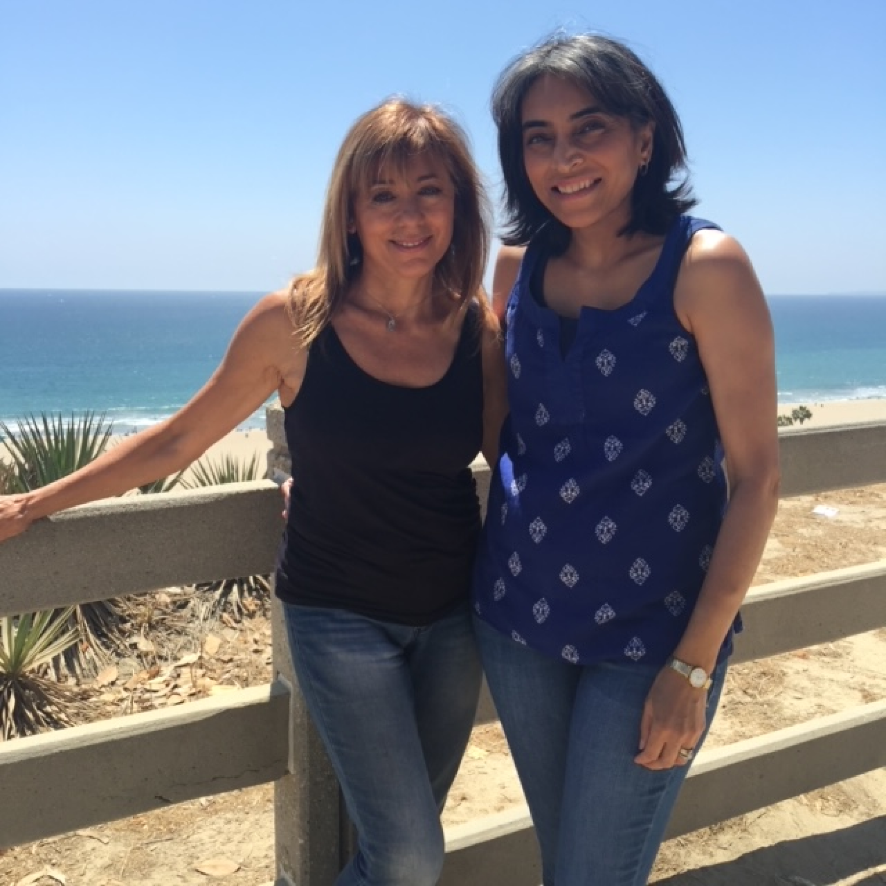 Two women standing next to each other with the ocean in the background