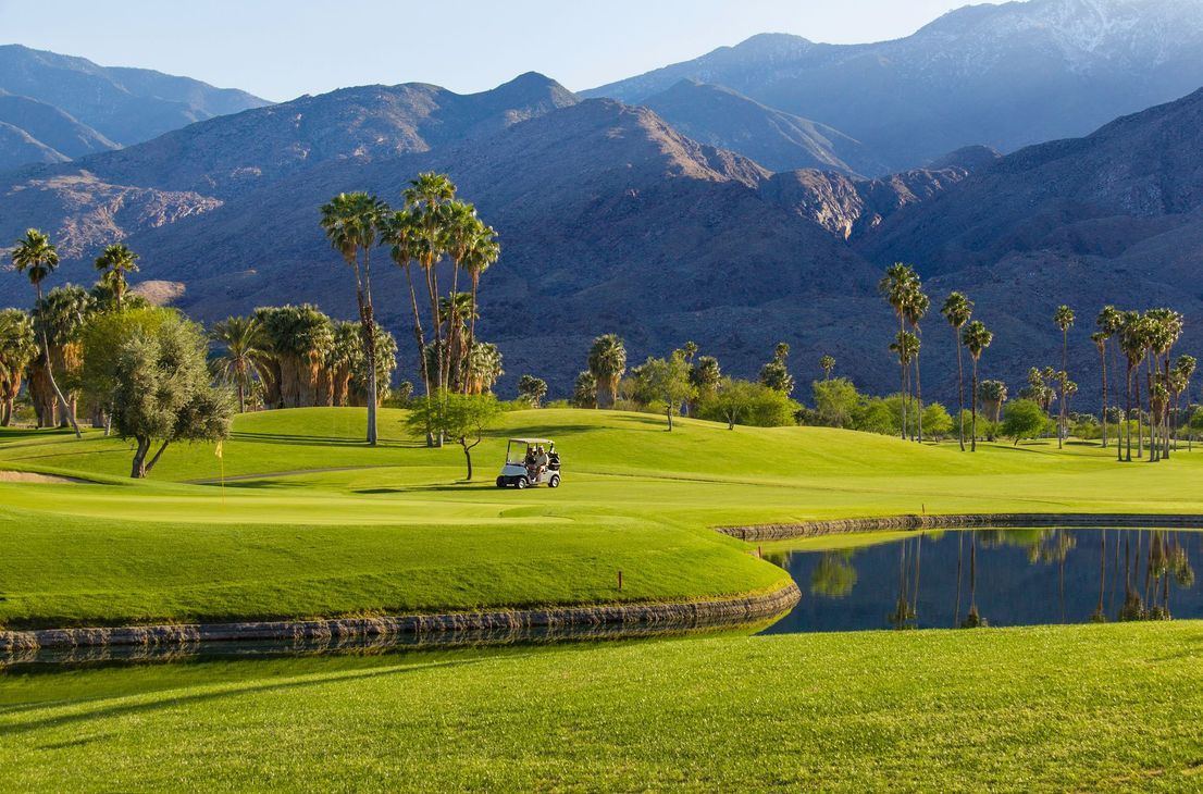 A golf course with palm trees and mountains in the background