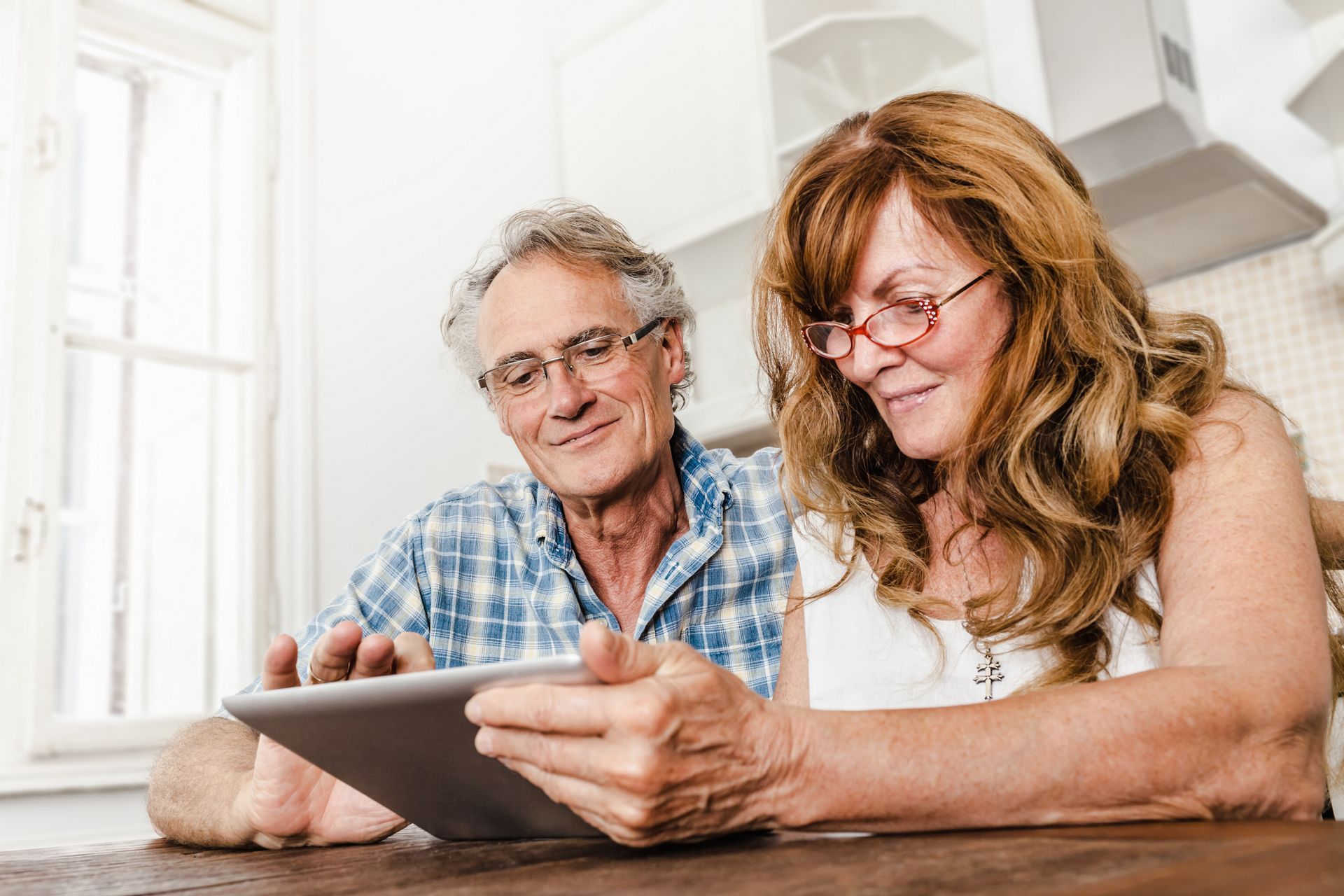 A man and a woman are sitting at a table looking at a tablet.
