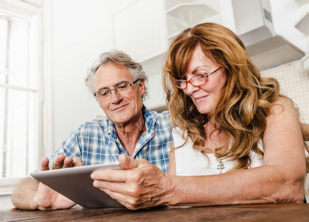 A man and a woman are sitting at a table looking at a tablet.