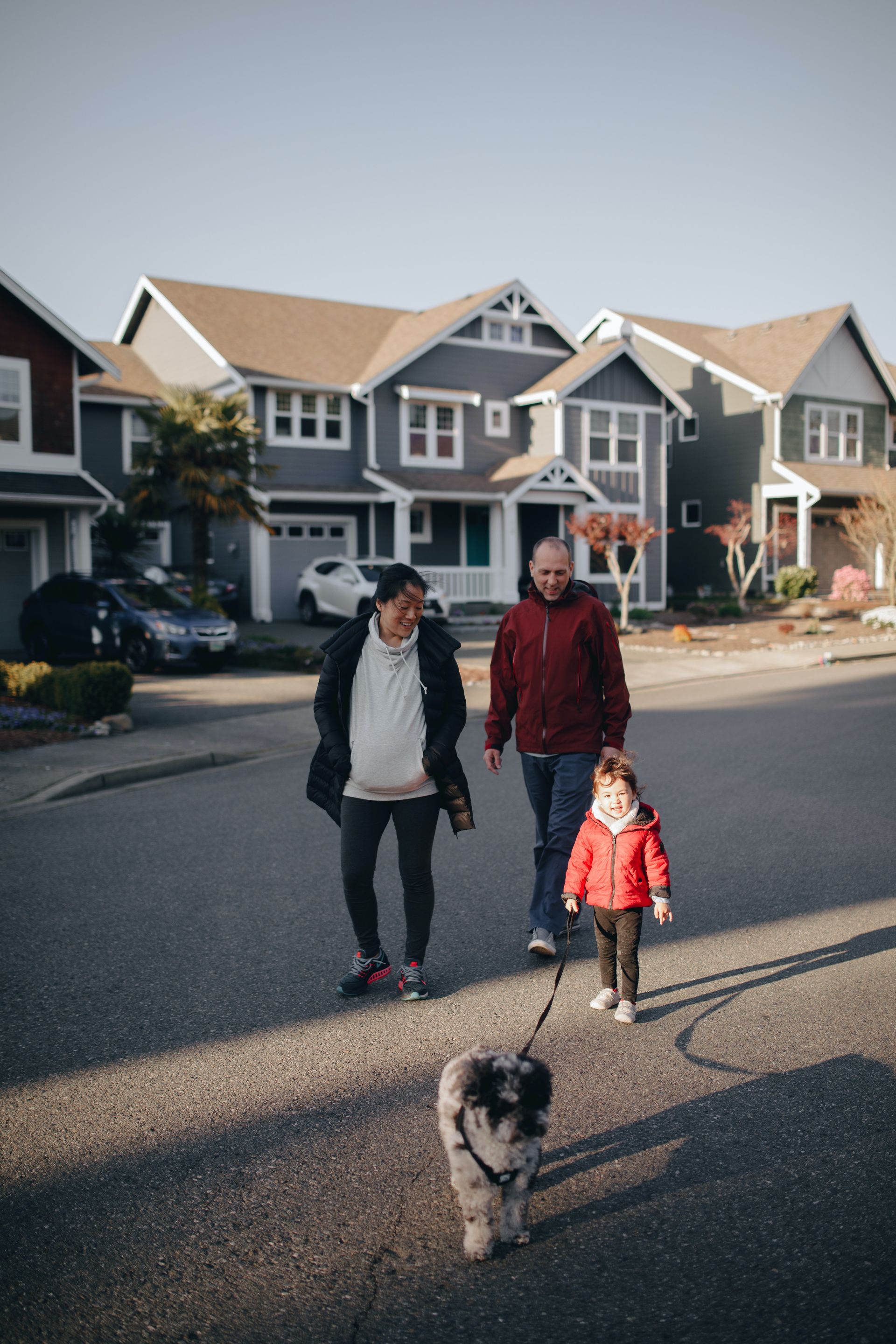 A family is walking a dog down a street in front of a house.