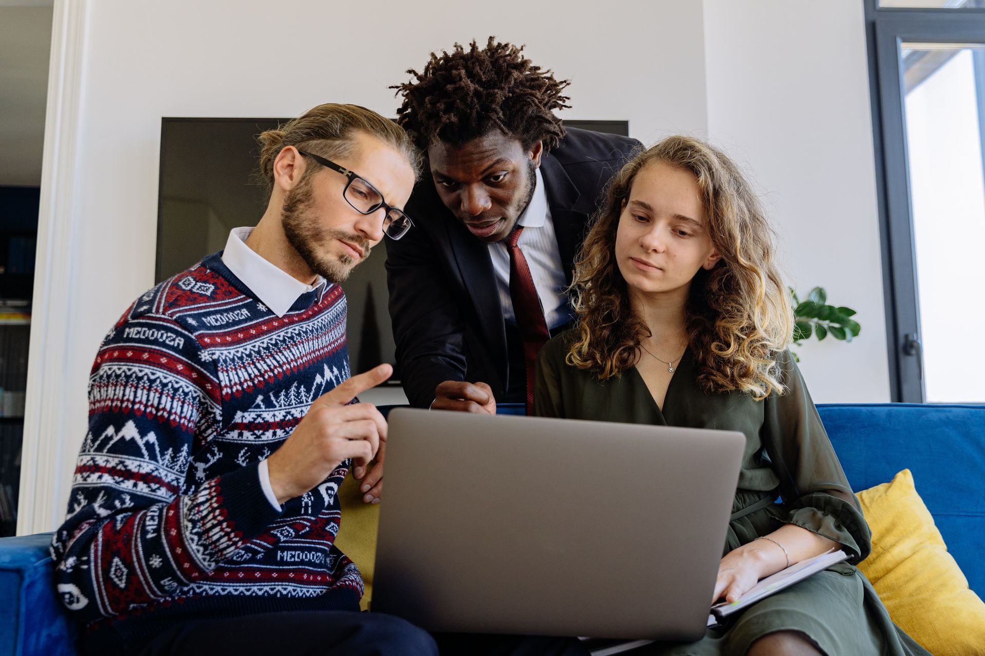 A group of people are sitting on a couch looking at a laptop computer.