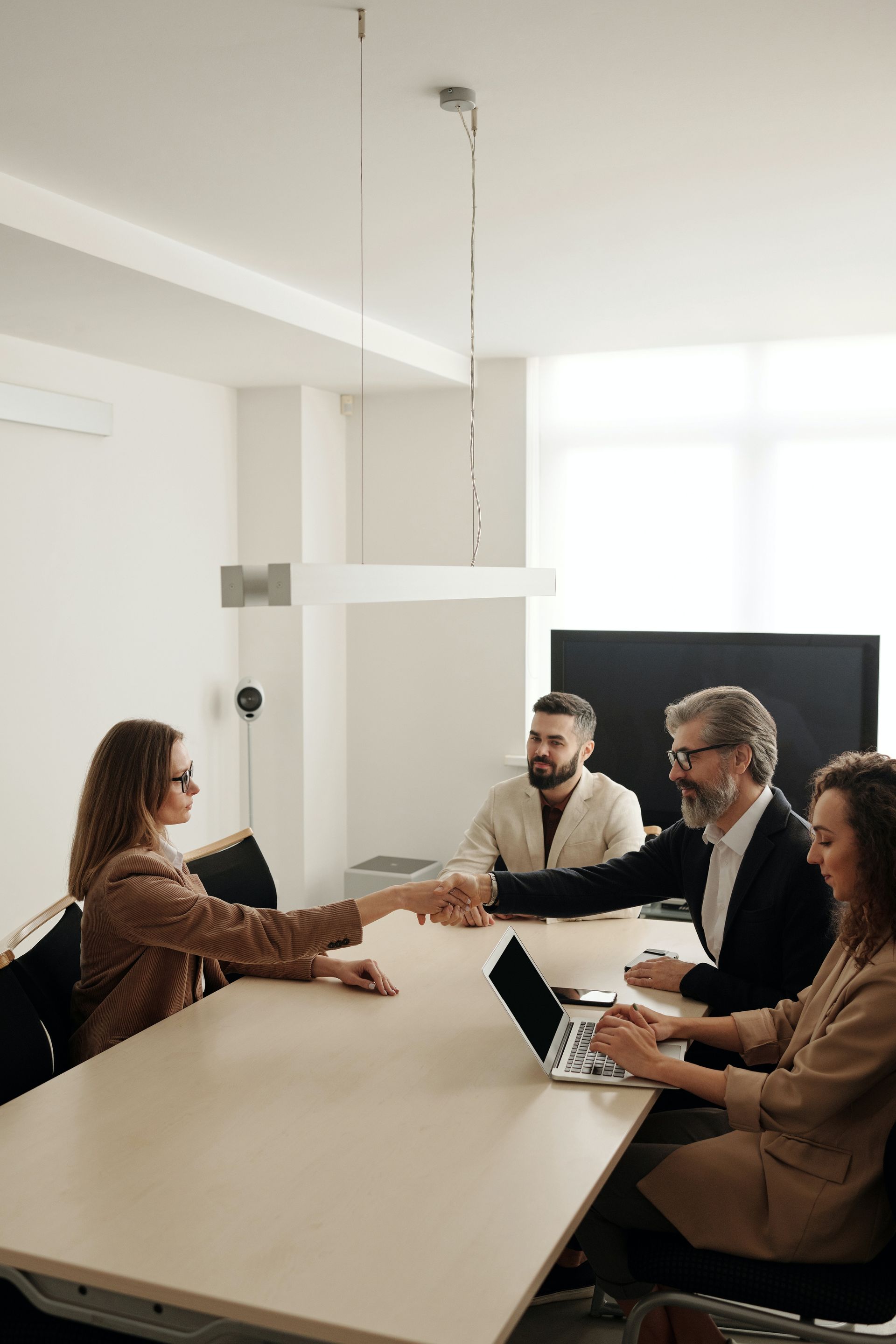 A group of people are sitting around a table shaking hands.