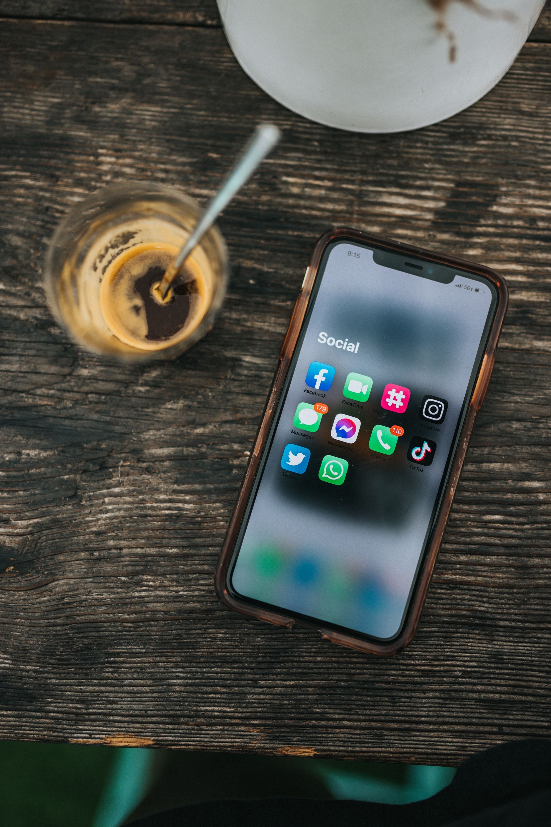 A cell phone is sitting on a wooden table next to a cup of coffee.