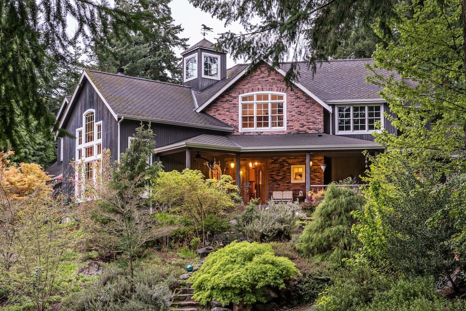 A large house with a porch is surrounded by trees and bushes.