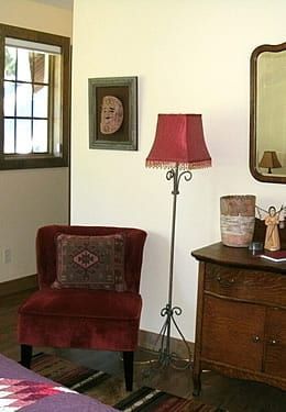 A living room with a chair , lamp , dresser and mirror.
