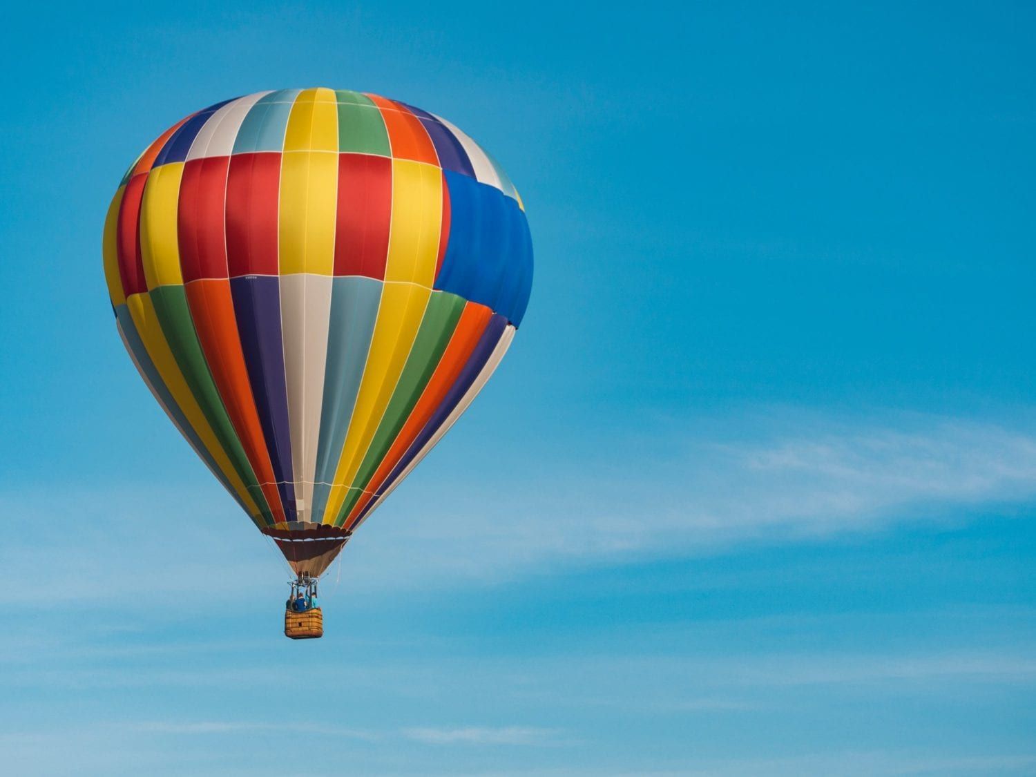 A colorful hot air balloon is flying in a blue sky.