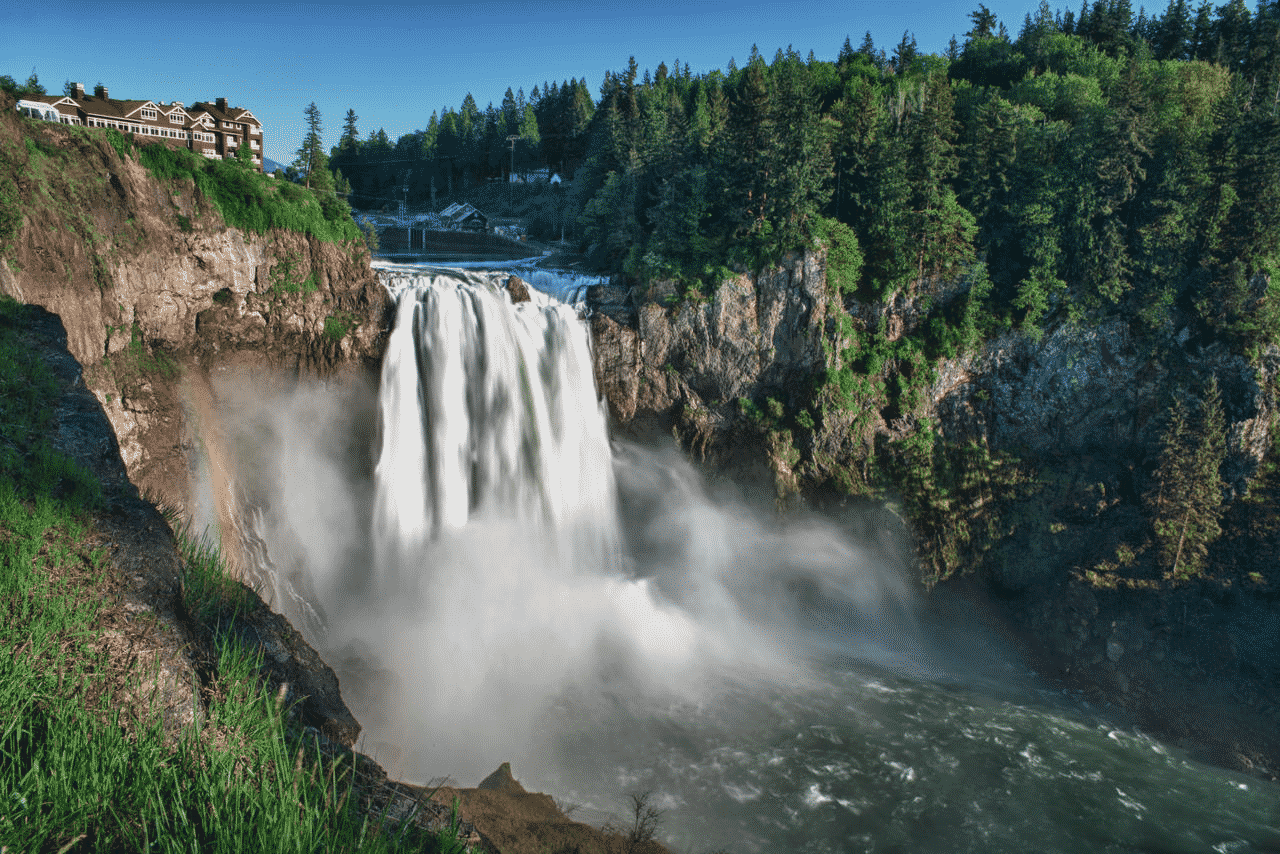 A waterfall is surrounded by trees and grass on a cliff.