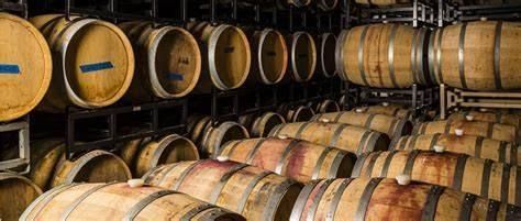 A row of wooden wine barrels stacked on top of each other in a wine cellar.