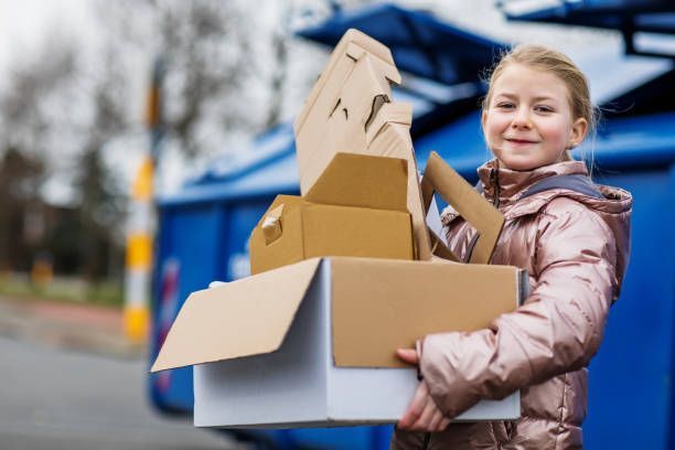 A young girl is holding a pile of cardboard boxes.