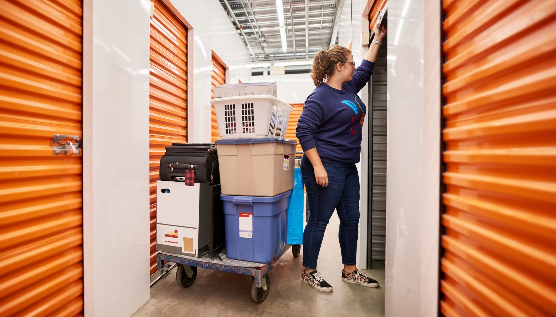 A woman is pushing a cart full of boxes in a storage unit.
