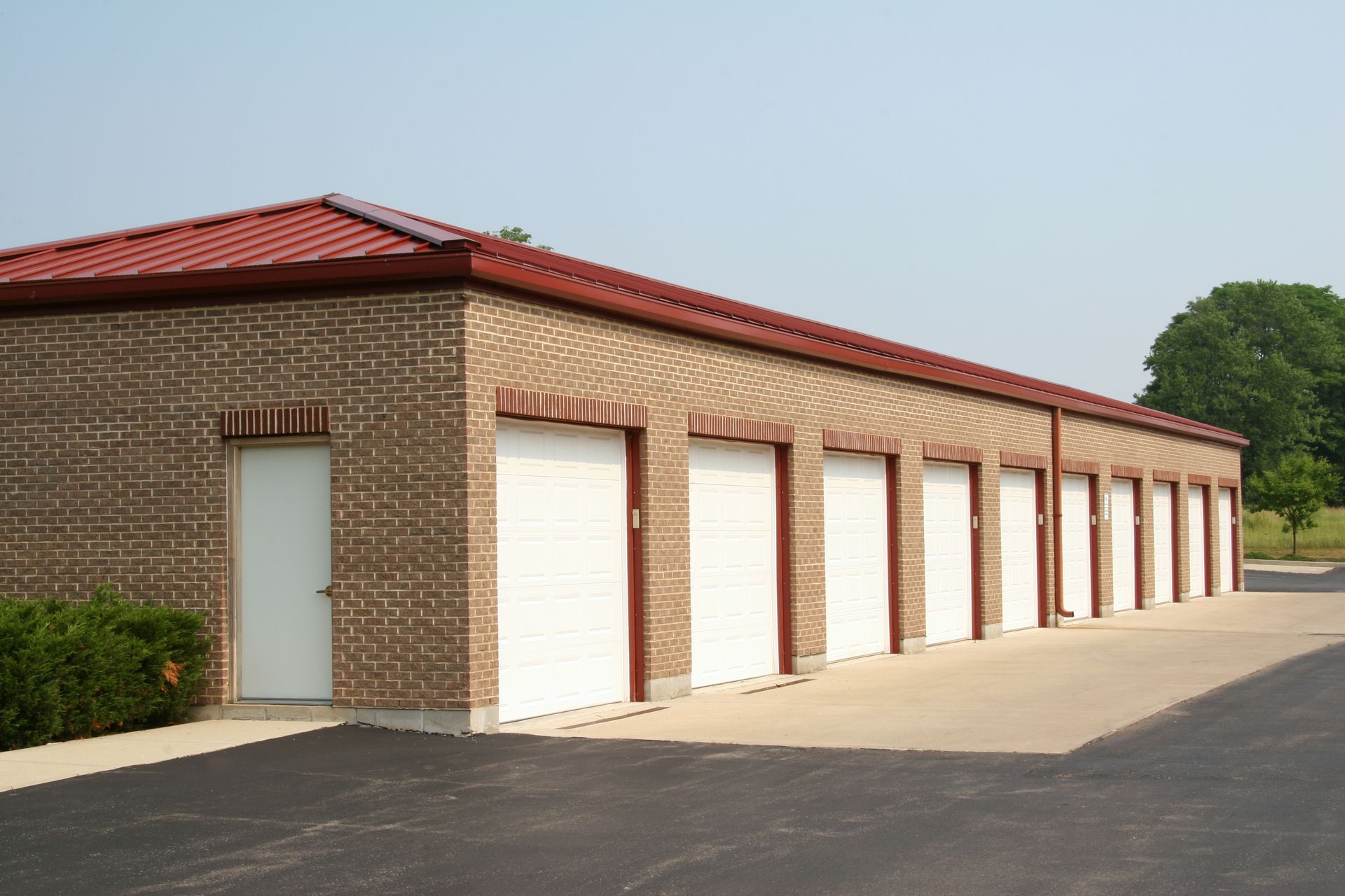 A row of brick garages with white doors and a red roof