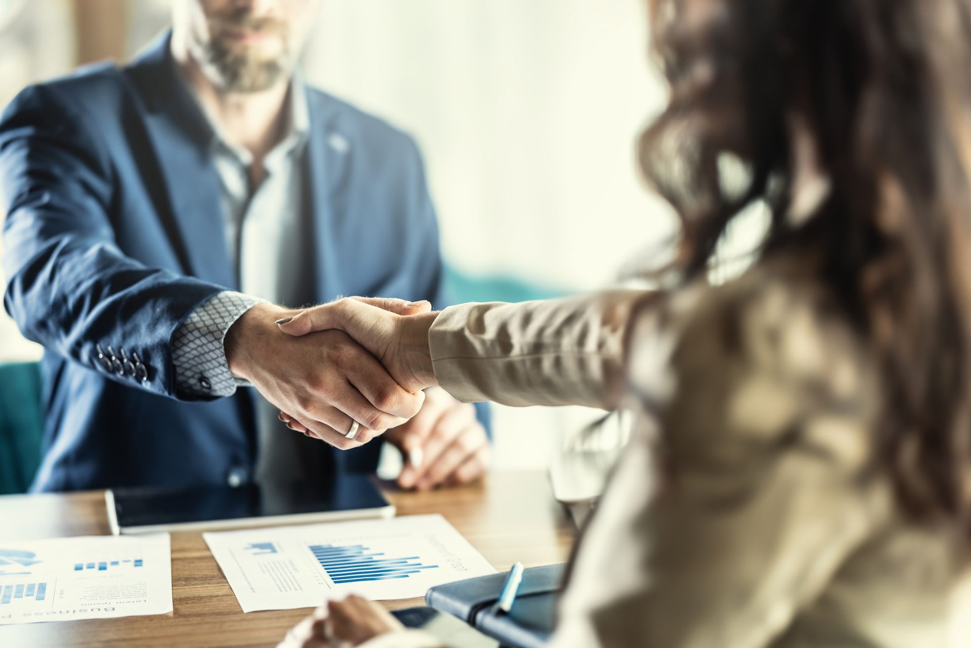 A man and a woman are shaking hands at a table.