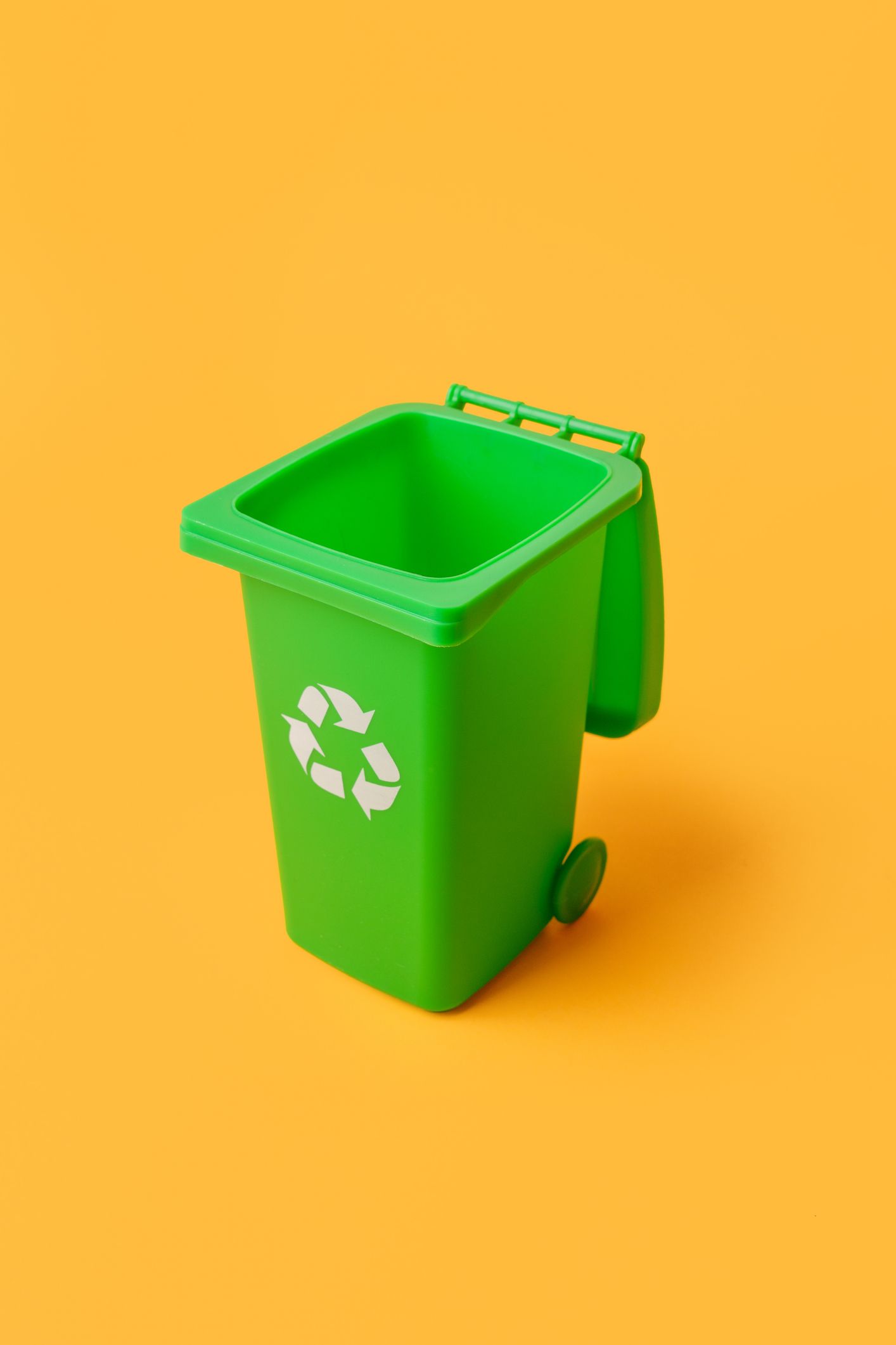 A green recycling bin with the lid open on a yellow background.