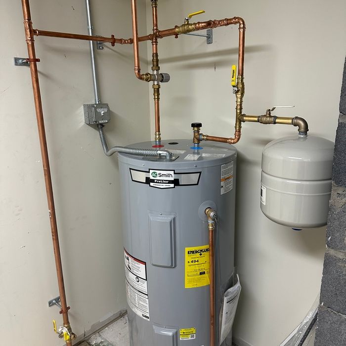 Copper pipes connected to a gray water heater, with an expansion tank nearby, in a utility room.