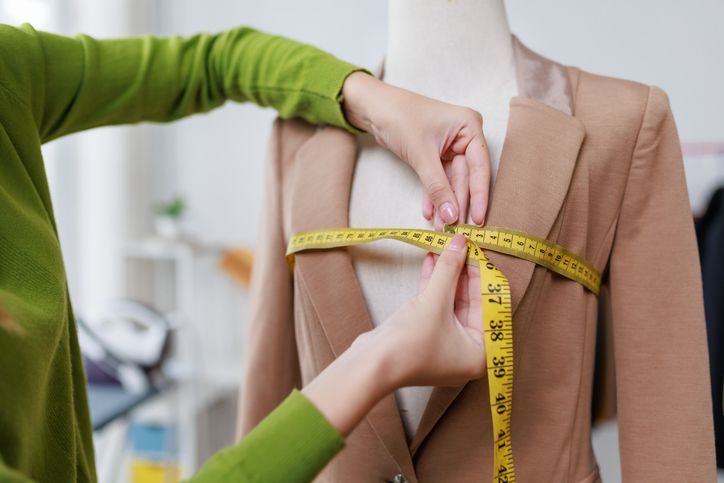 Una persona mide un blazer color canela sobre un maniquí con una cinta métrica amarilla en un estudio de sastrería.