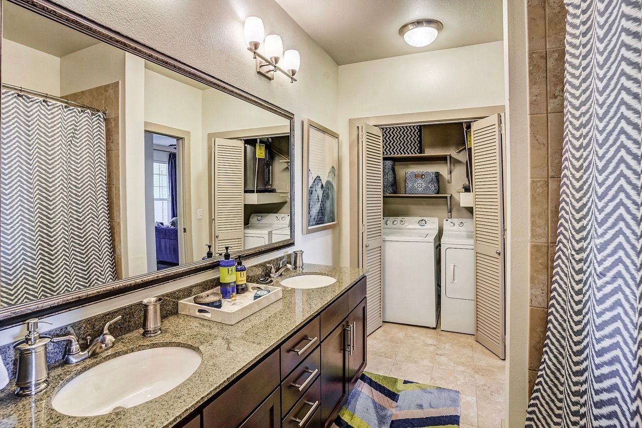 Bathroom vanity with double sinks and a closet housing a washer and dryer.