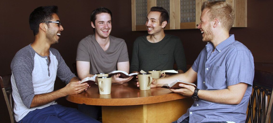 A group of men are sitting around a table reading books and drinking coffee.