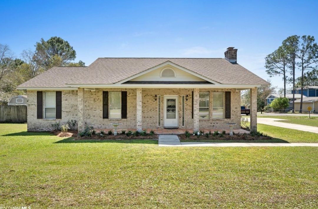 A brick house with a porch and a lot of grass in front of it.