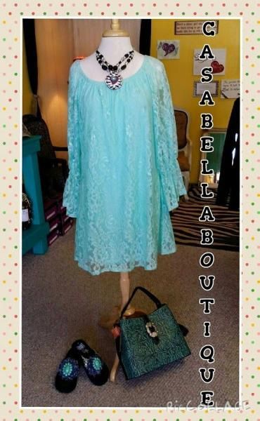 Light aqua embellished dress with matching necklace, handbag, and black shoes displayed on a boutique wall