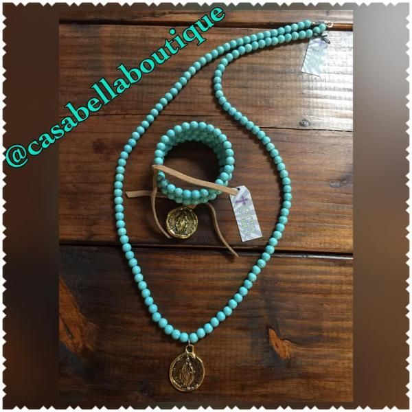 Turquoise beaded necklace and bracelet with gold pendants on a wooden surface