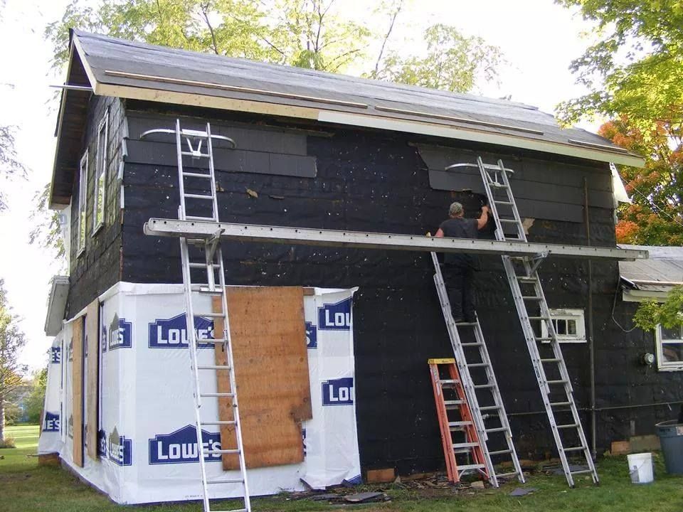 A man is working on the side of a house that is covered in lowe 's siding