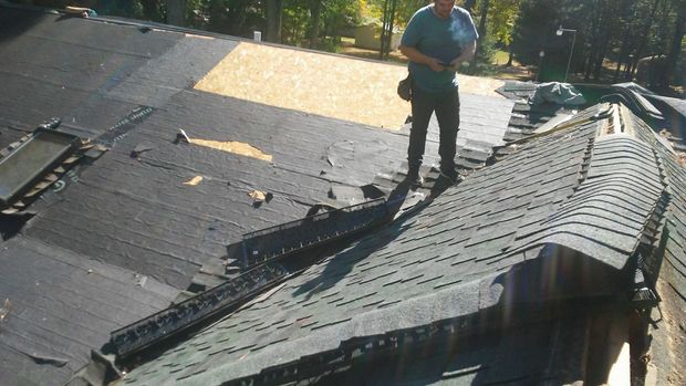 A man is standing on top of a black roof