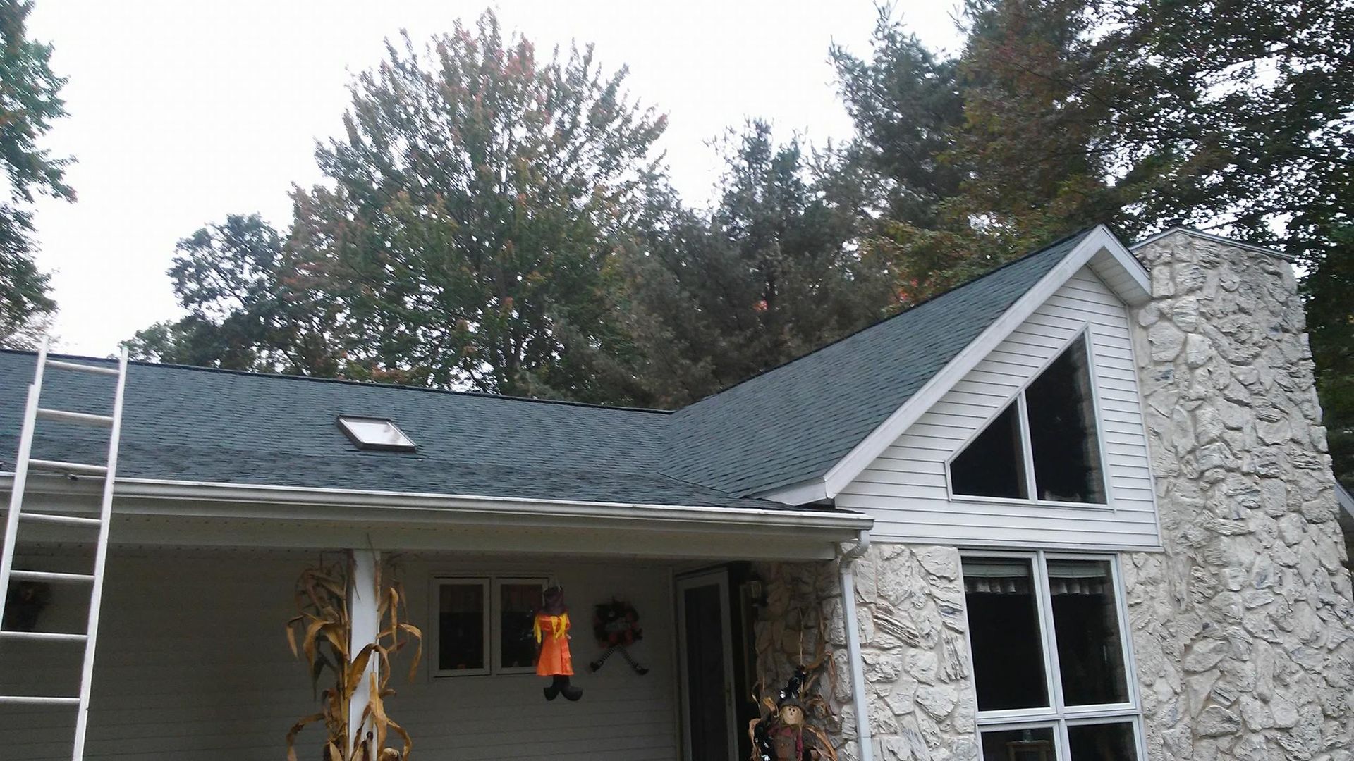 A white house with a black roof and a ladder on the porch.