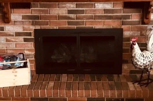 Brick fireplace with black doors, wooden mantle, and rooster statue.