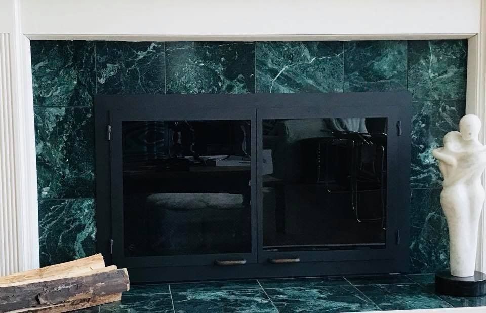 Fireplace with black glass doors set against green marble. A white sculpture and logs are nearby.