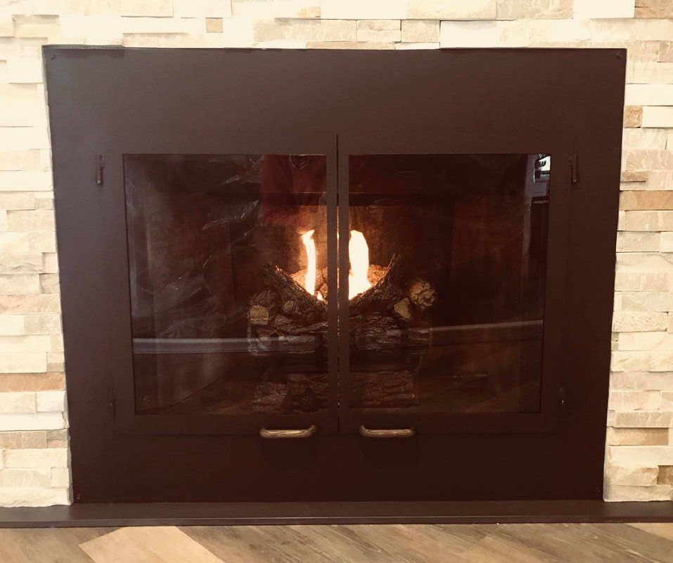 Fireplace with glass doors and burning flames, set in a stone wall.
