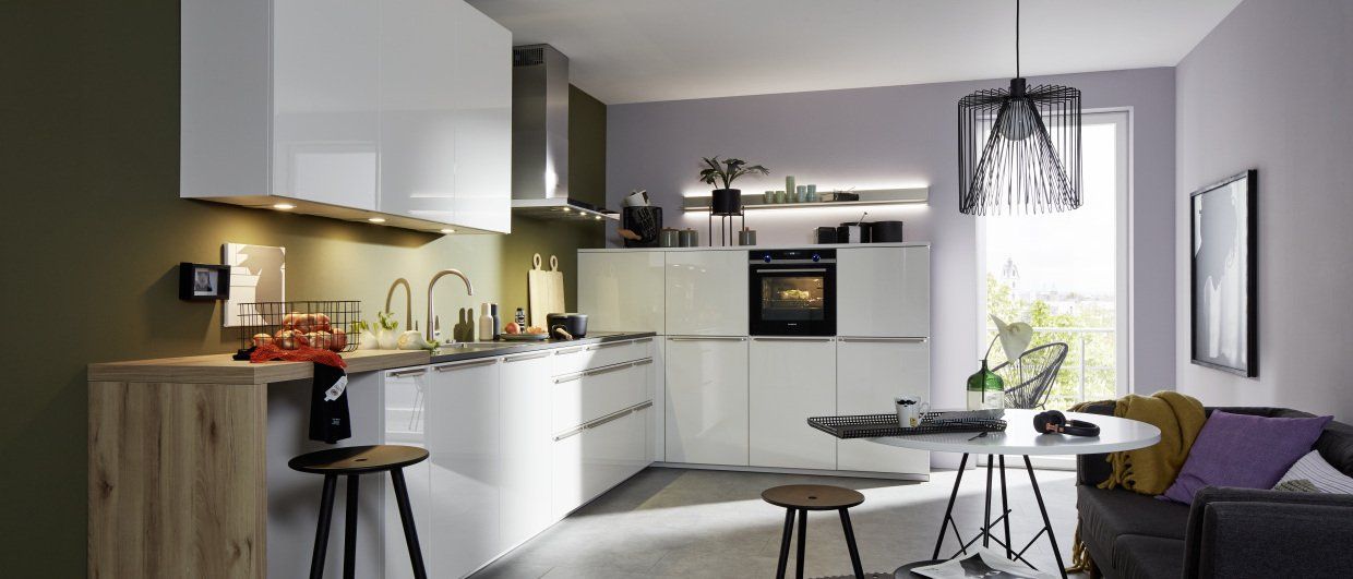 Une cuisine avec des armoires blanches, des tabourets, une table et un canapé.